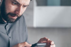 Mann Ende Dreißig, Anfang Vierzig blickt skeptisch und irritiert auf sein Smartphone