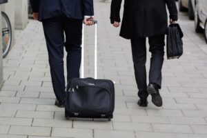 Zwei Männer in Anzügen gehen mit einem Rollkoffer durch eine Stadtstraße