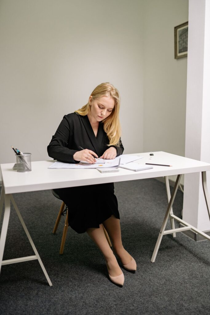 Junge blonde Frau in elegantem Outfit unterschreibt Dokumente an einem Schreibtisch